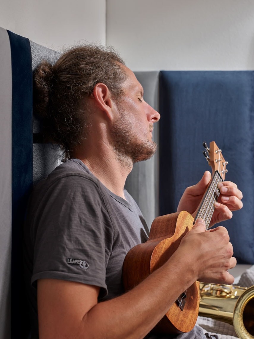 Mężczyzna gra na instrumencie i opiera się o panele tapicerowane w szarym i granatowym kolorze