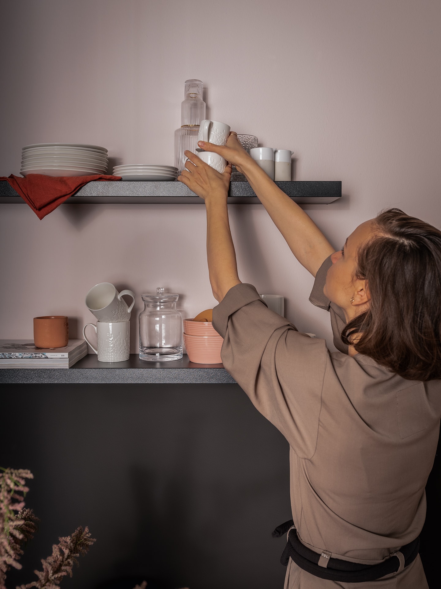 Ciemne półki, na których kobieta ustawia ceramikę