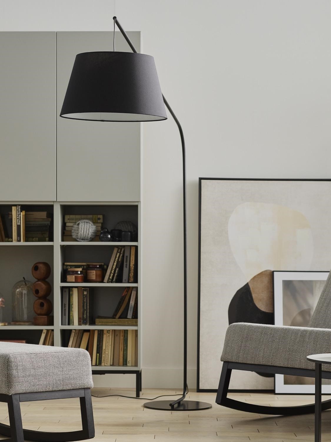 Czarna, minimalistyczna lampa podłogowa w salonie, obok regału z książkami .