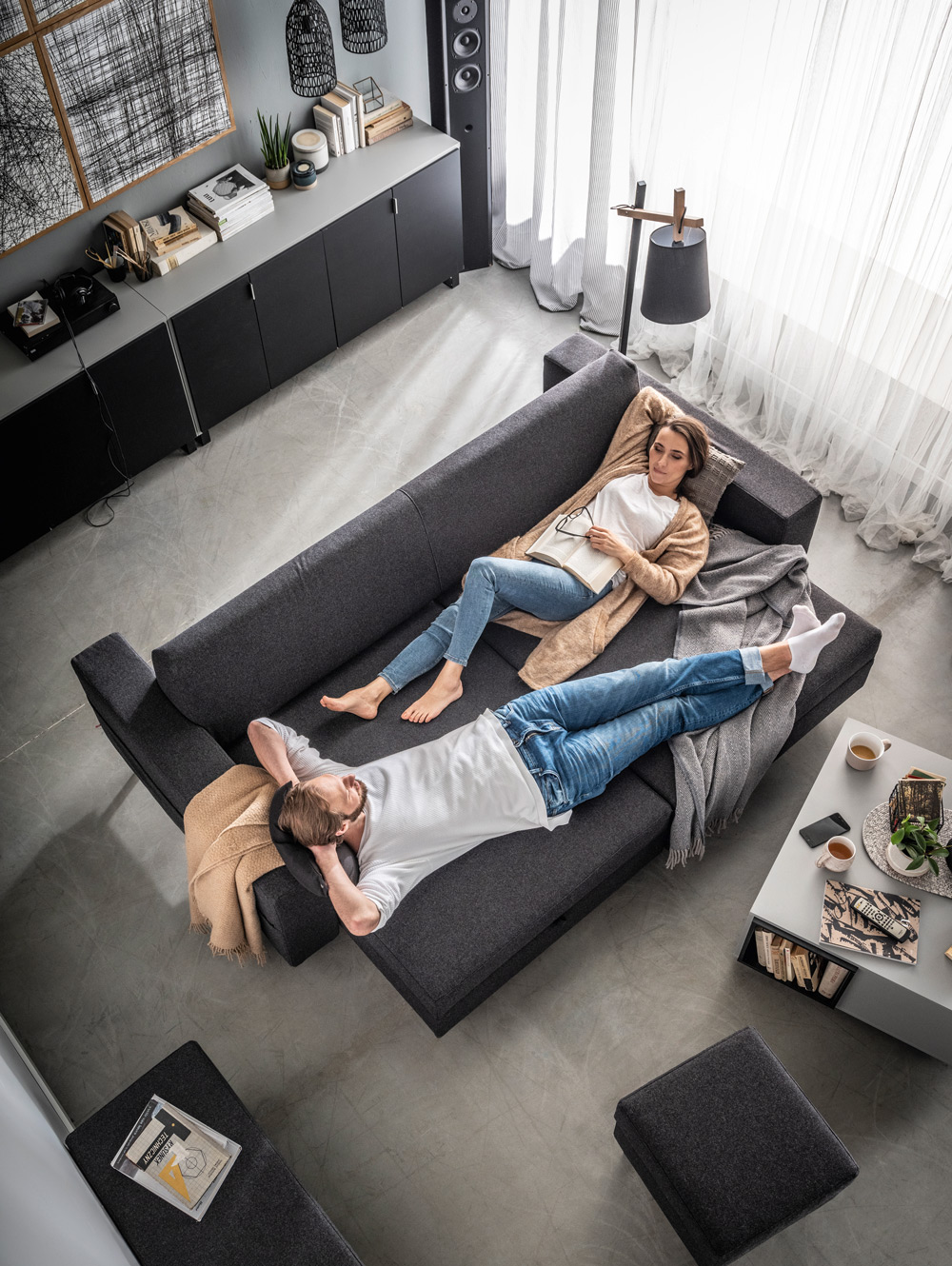 Ciemnoszara sofa z funkcją spania, na której relaksuje się para.