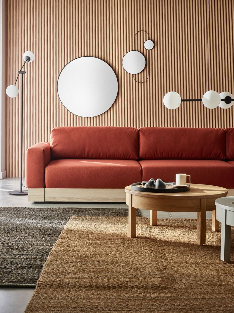 Ceglasta sofa na tle lameli z okrągłymi lustrami w jasnym salonie