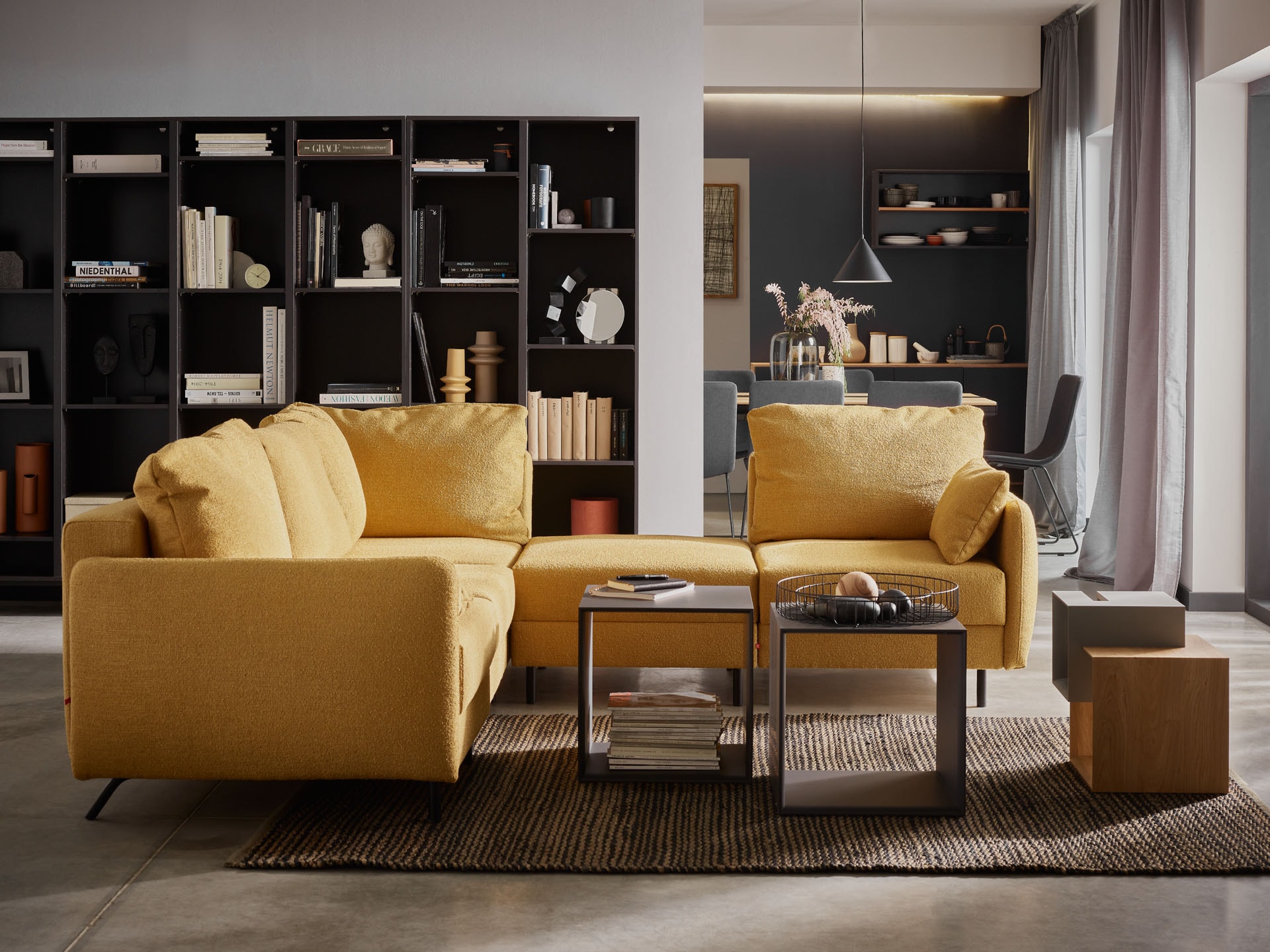Musztardowa sofa, czarny regał na tle białych ścian