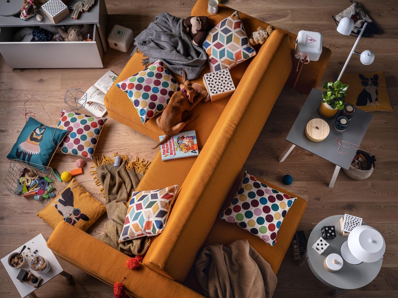 Przytulne wnętrze z pomarańczową sofą i kolorowymi poduszkami w geometryczne wzory.