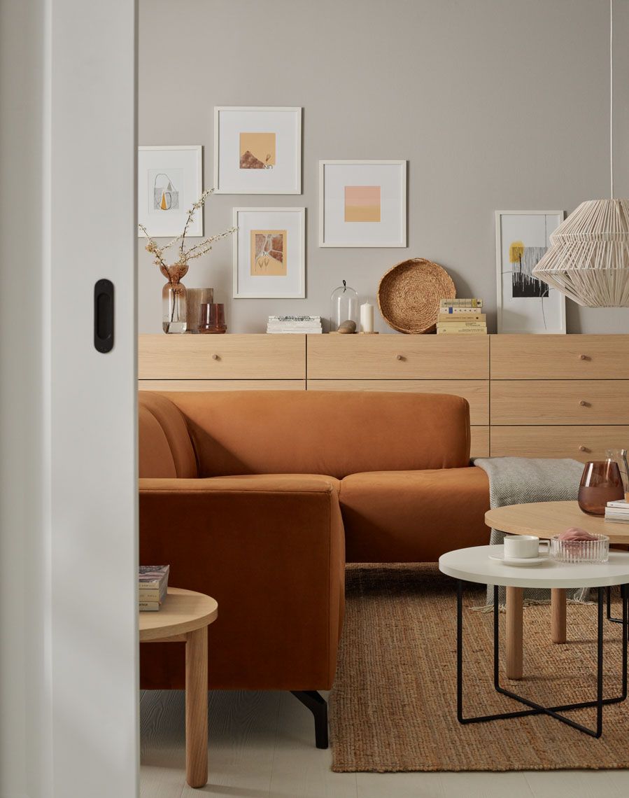 Przytulny salon z rdzawą sofą, naturalnym dywanem i galerią obrazów nad komodą.