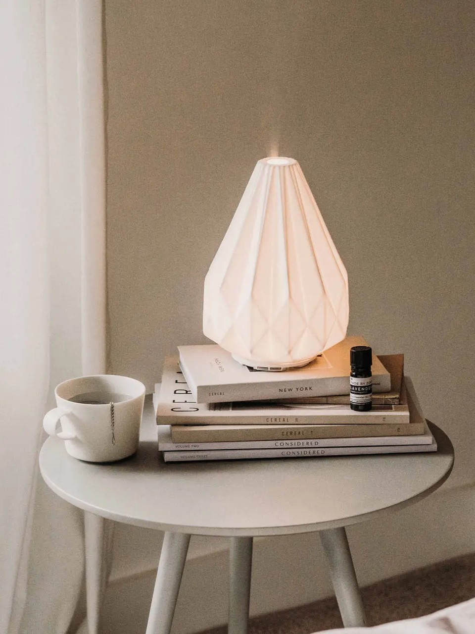 Ceramiczny dyfuzor na stosie książek i filiżanka z herbatą na minimalistycznym stoliku