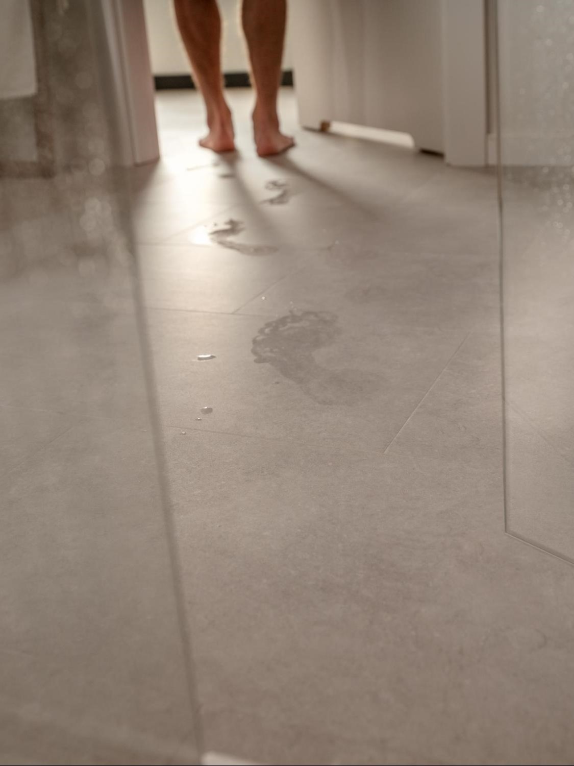 Zbliżenie na podłogę w stylu betonu w łazience z mokrymi śladami, podkreślające jej odporność na wilgoć.