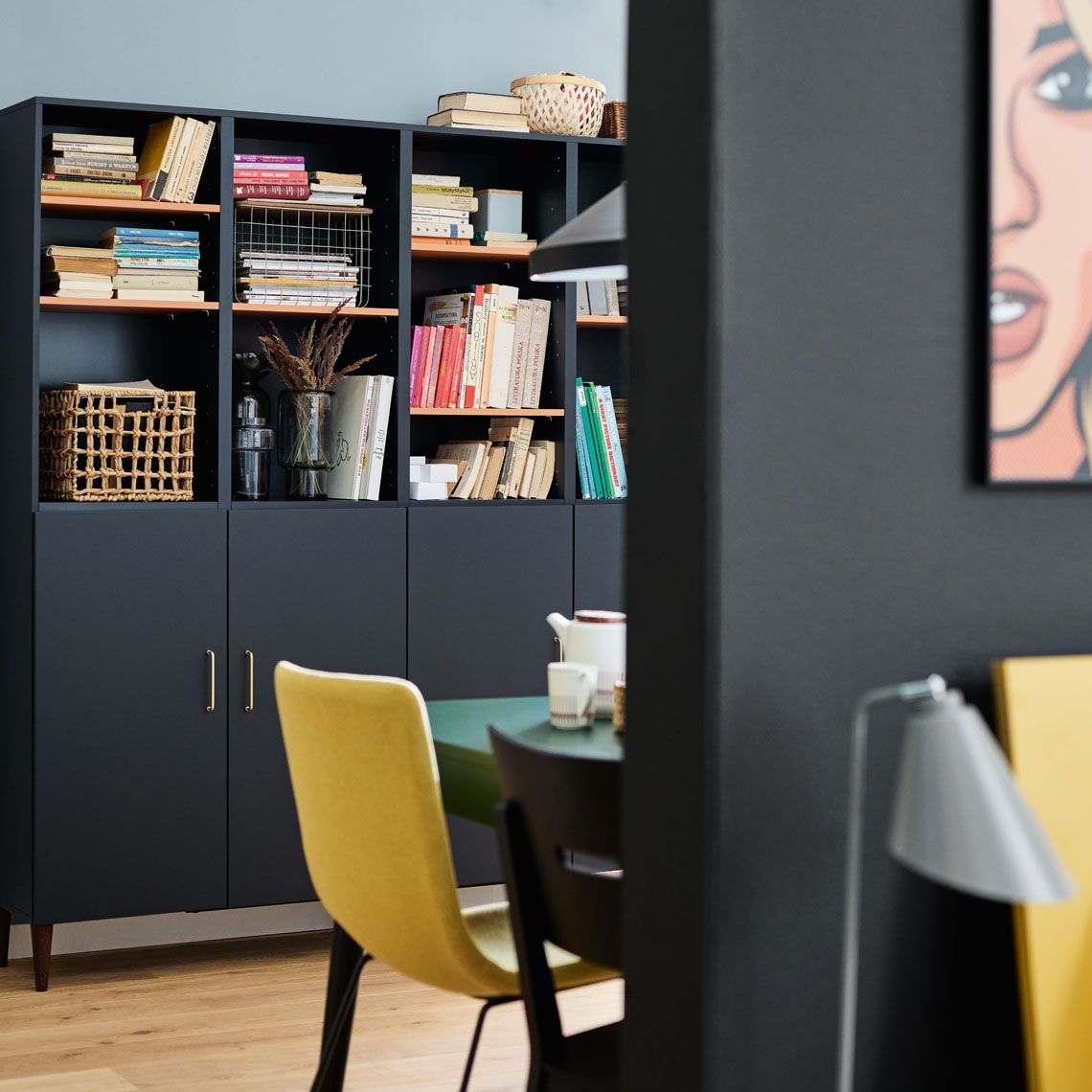 Designerska jadalnia z czarną biblioteczką, żółtym krzesłem i grafiką pop-art 