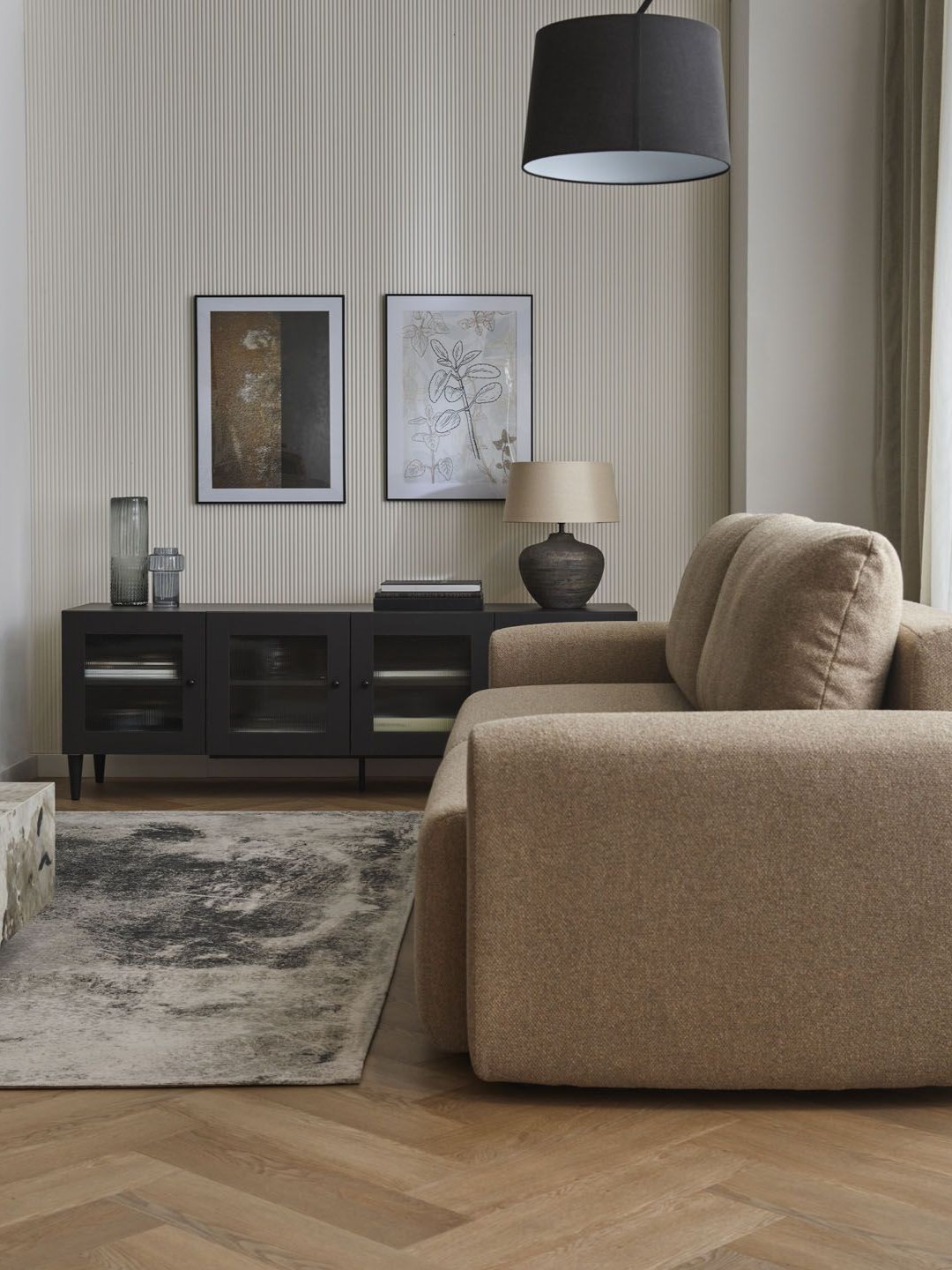 Beżowa sofa na tle lameli i czarnej komody z obrazami