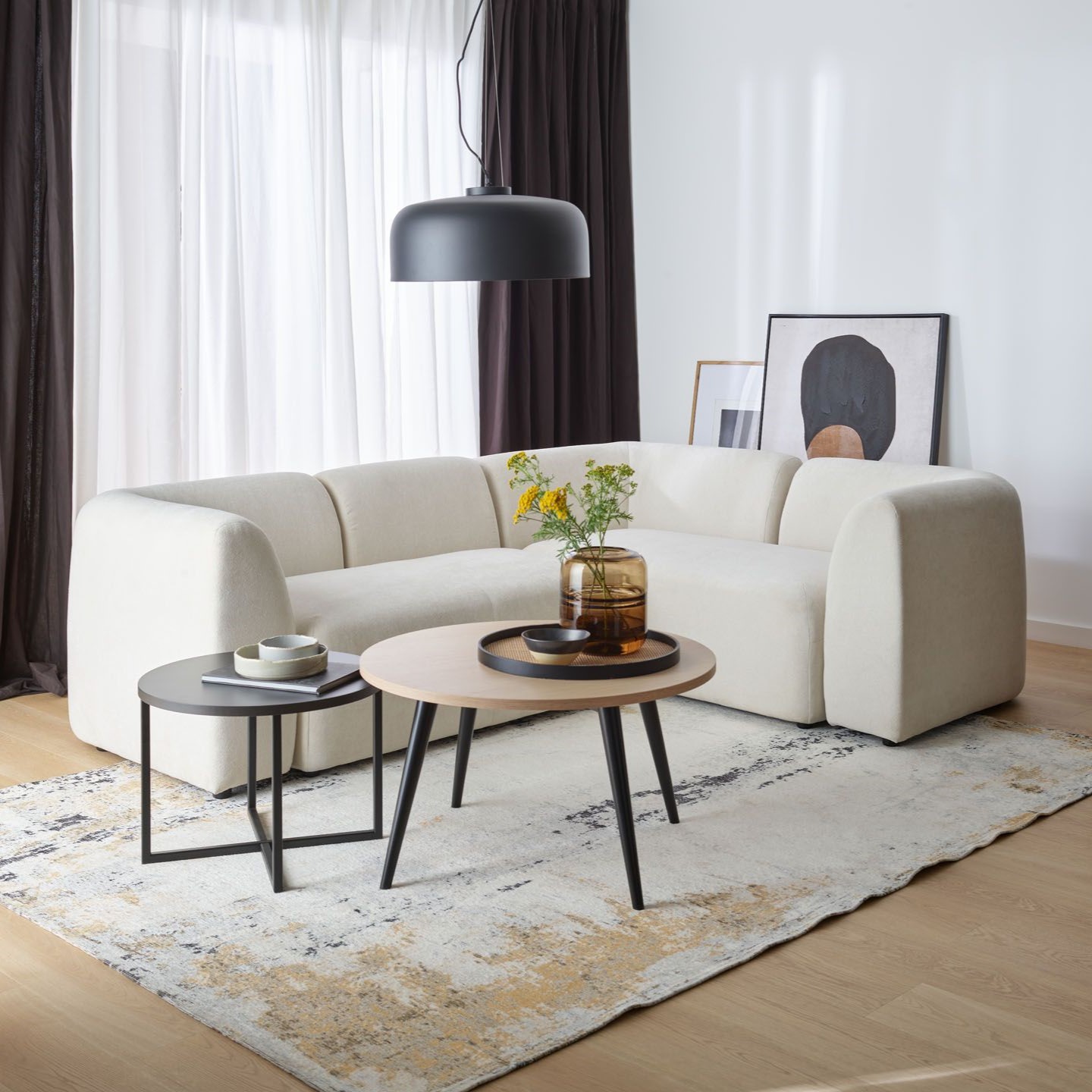 Elegancki salon z jasną sofą i dużą czarną lampą wiszącą nad stolikami kawowymi.