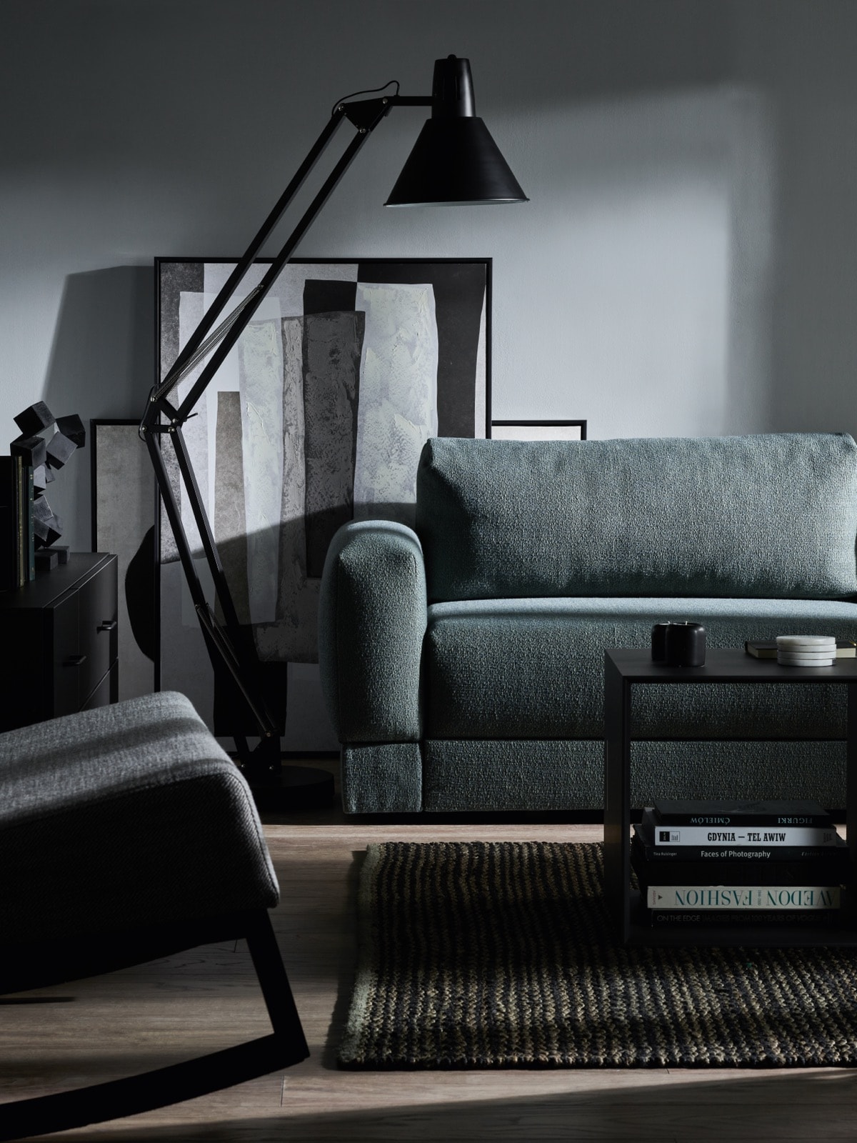 Ciemnoszara sofa i czarna lampa podłogowa na tle szarej ściany