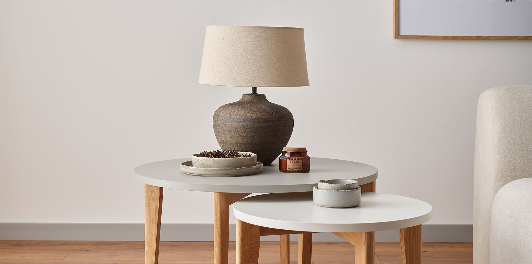 Stonowana lampa stołowa z ceramiczną podstawą i beżowym kloszem, ustawiona na zestawie okrągłych stolików,