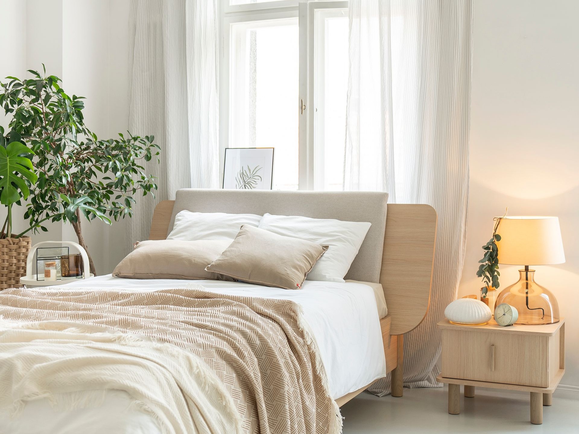 Naturalne materiały i jasne kolory – przytulna aranżacja małej sypialni z rośliną i drewnianym łóżkiem.