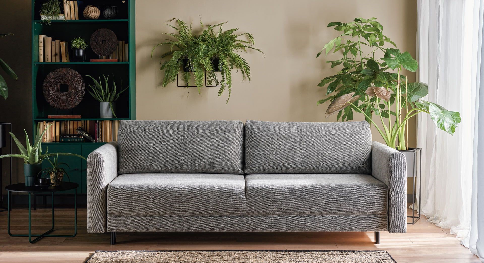 szara sofa w salonie otoczona roślinami doniczkowymi