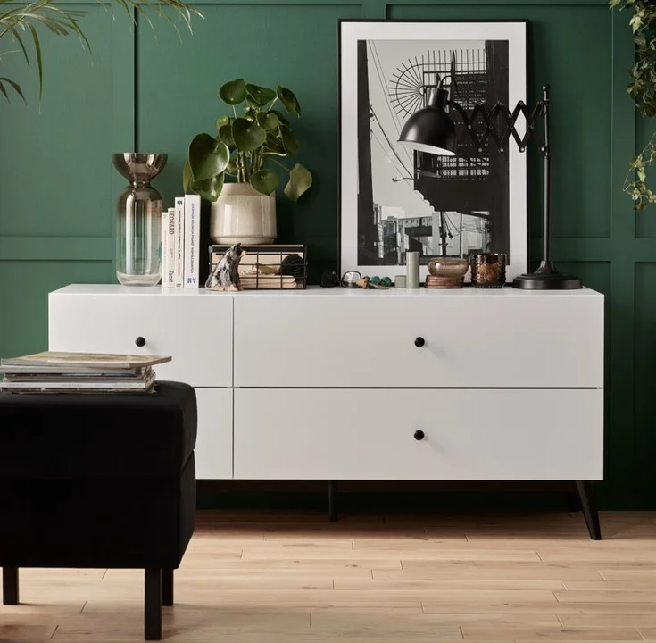 elegancki salon z zieloną boazerią i białą komodą 