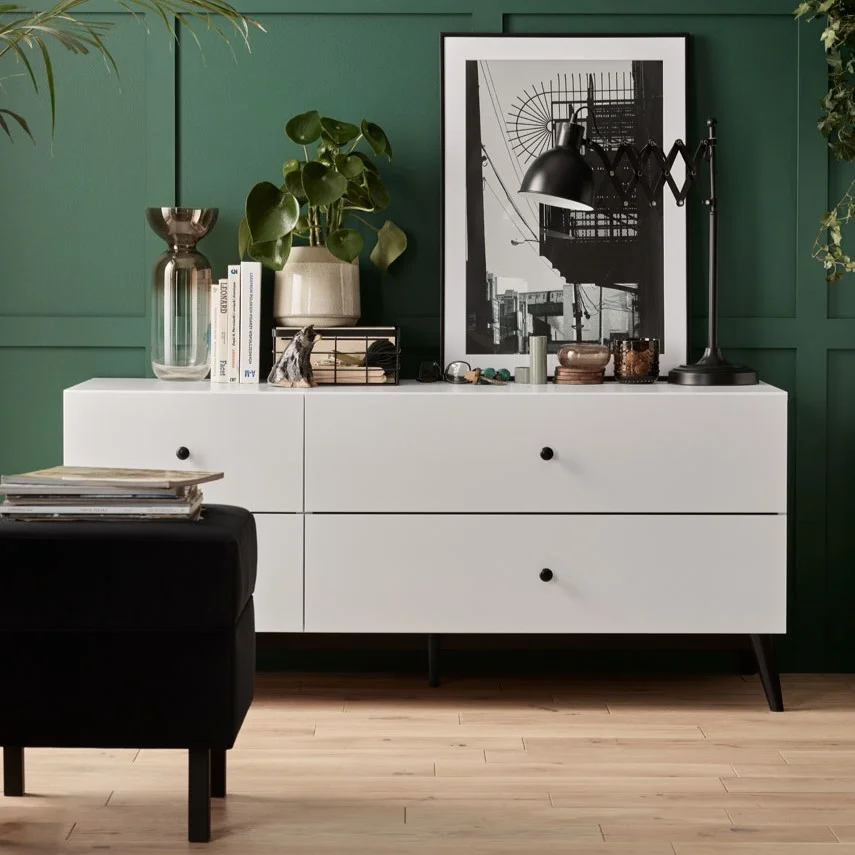 elegancki salon z zieloną boazerią i białą komodą 