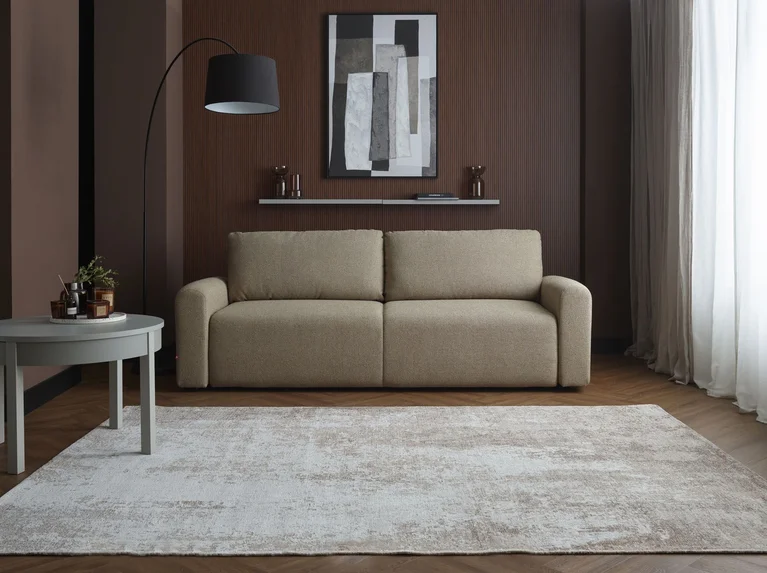 Oliwkowa sofa Fika na tle czekoladowej ściany