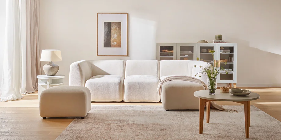 Jasny, przestronny salon z wygodną, kremową sofą o zaokrąglonych kształtach, stolikiem kawowym i subtelnymi dekoracjami, tworzy eleganckie i minimalistyczne wnętrze.