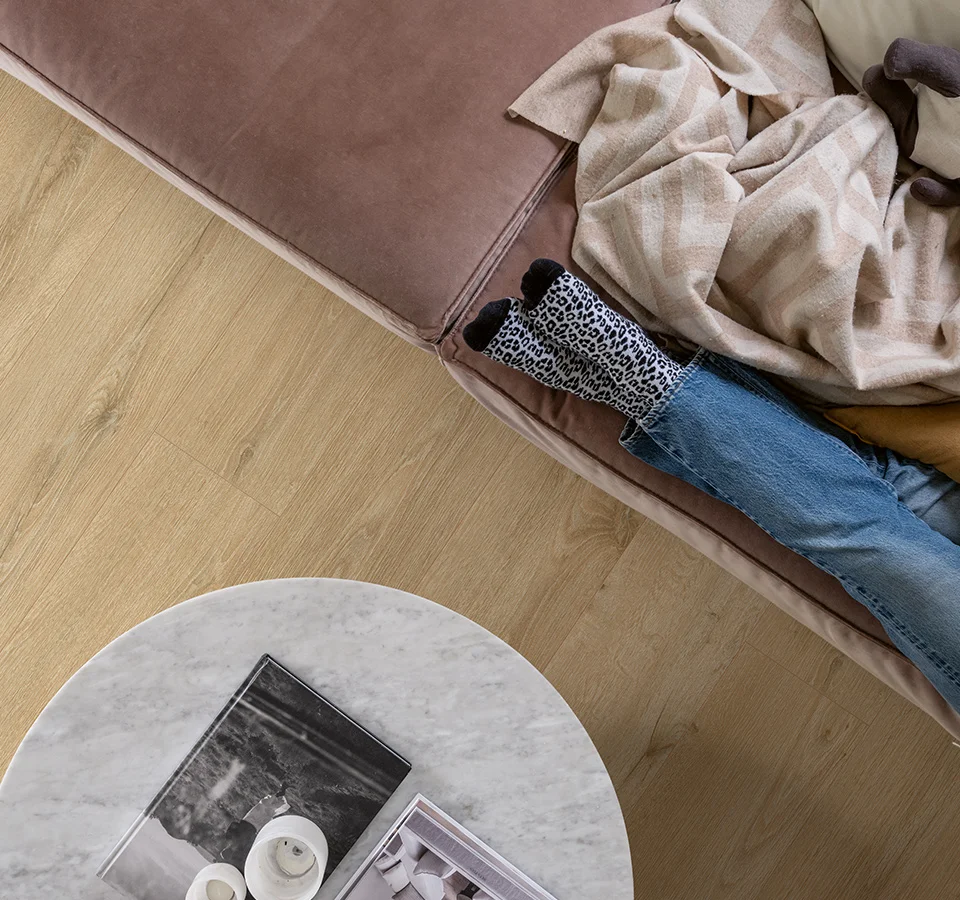 ciepła, drewniana podłoga i wygodna sofa, na której mama czyta książkę obok śpiącej córki.